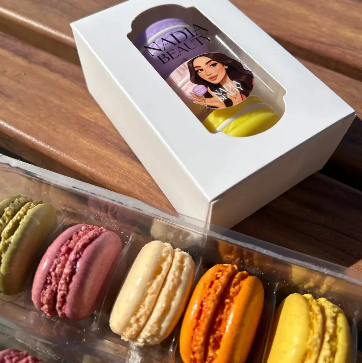 Box of colorful macarons with a visible brand logo on a wooden surface
