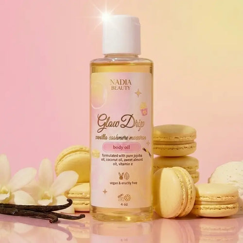 Nadia Beauty Glow Drop body oil bottle with macarons and flowers on a pink background